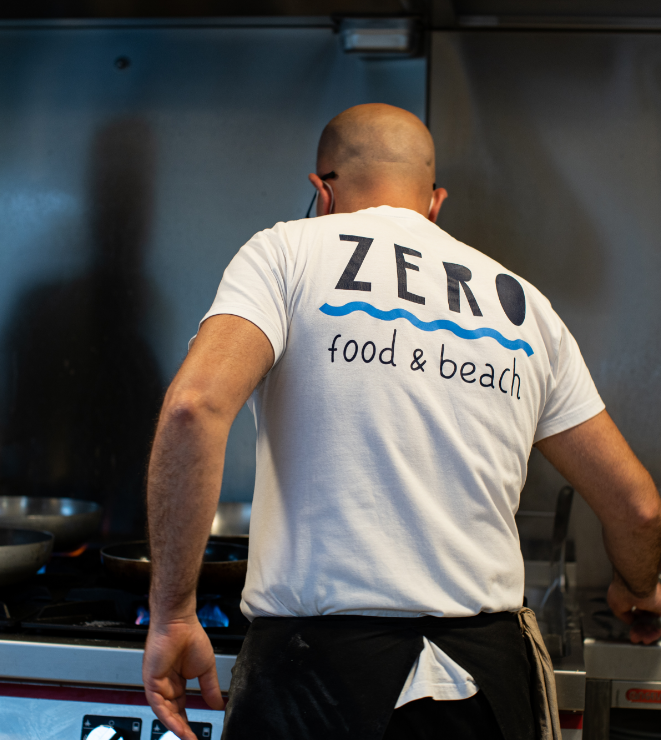 kitchen worker from behind wears T-shirt with Zero Food and beach written on it
