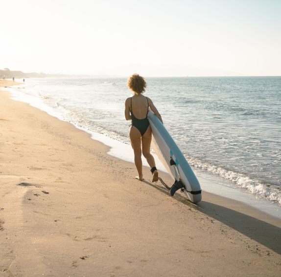 ragazza di spalle, che cammina sulla riva con tavola da surf